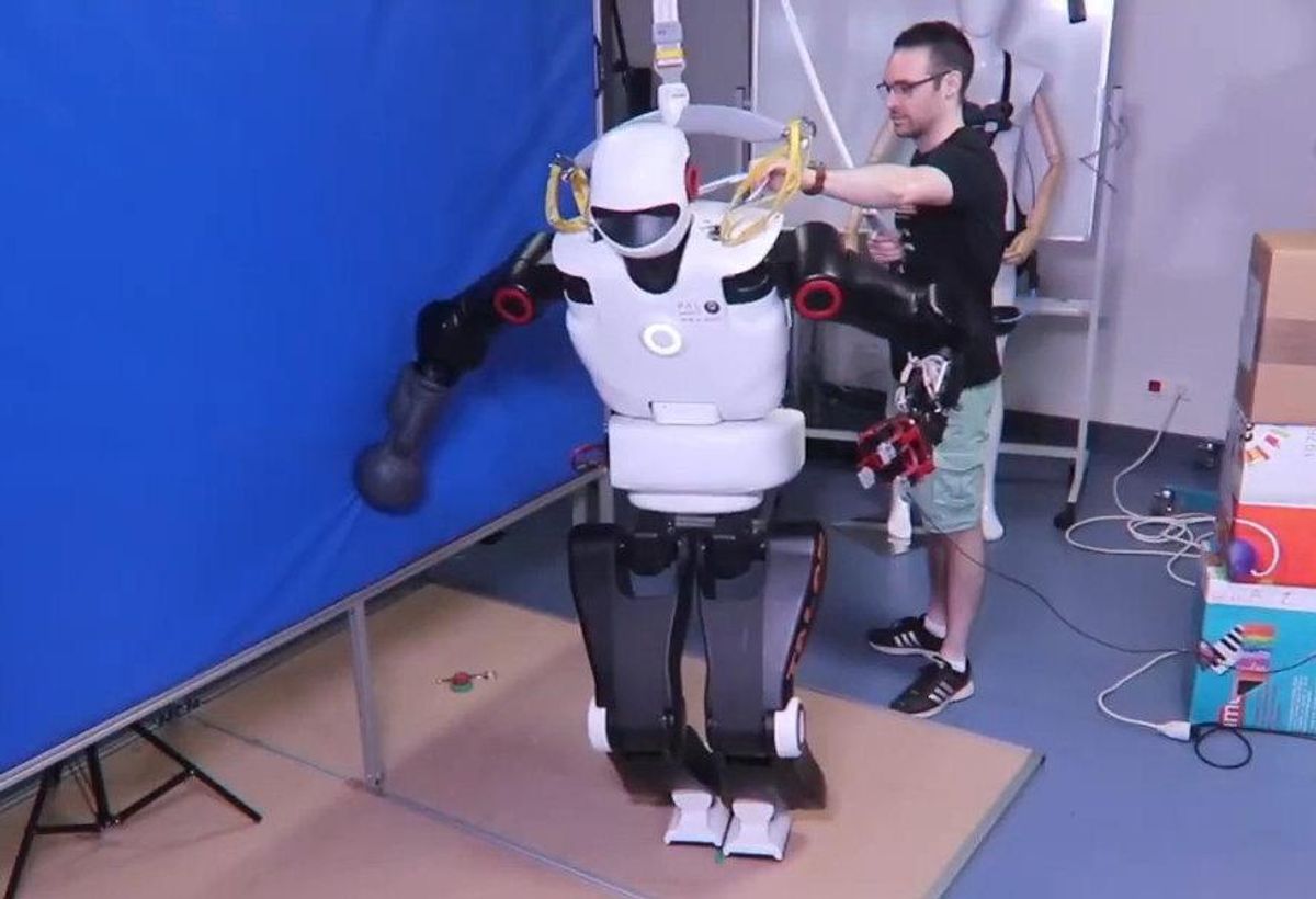 一个黑白相间的人形机器人有一条腿出了故障，一只手臂靠在墙上支撑着自己