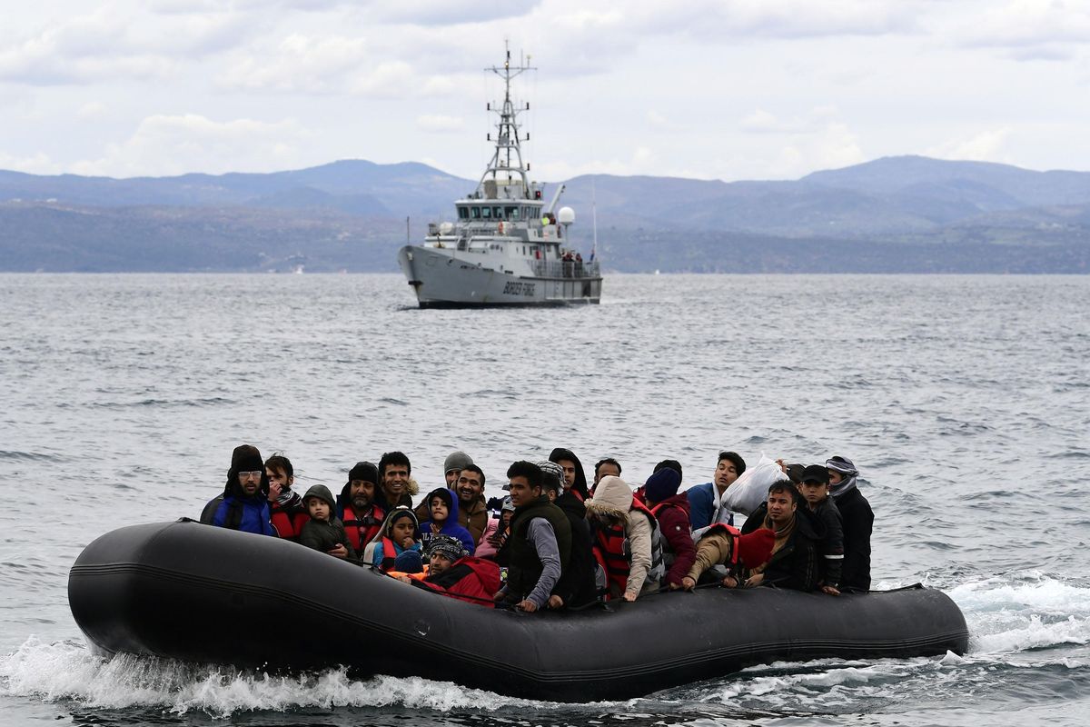 一群人坐在水面上的充气船上，背景是一艘巡逻舰。