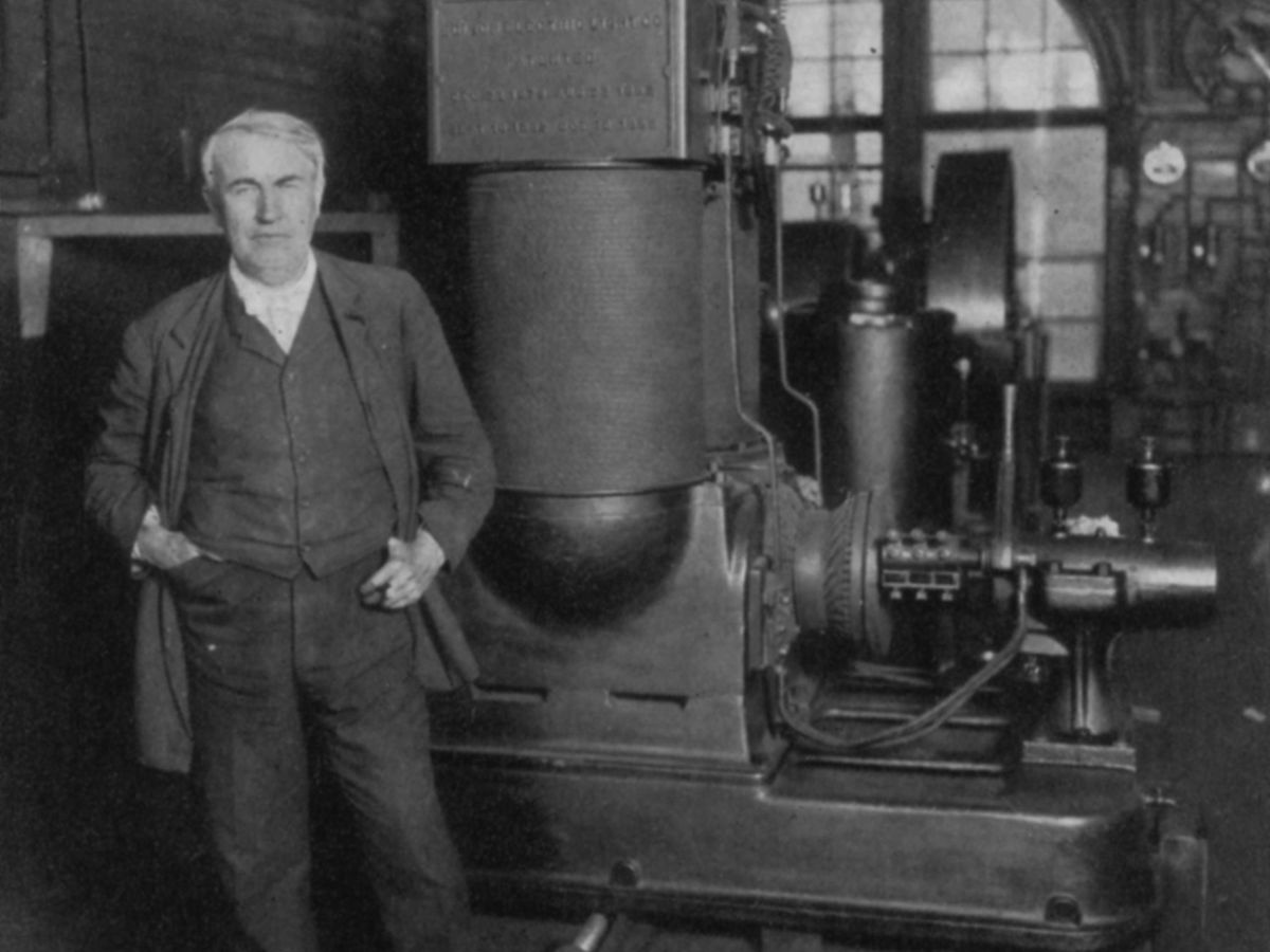 托马斯·阿尔瓦·爱迪生站在发电机前的照片。