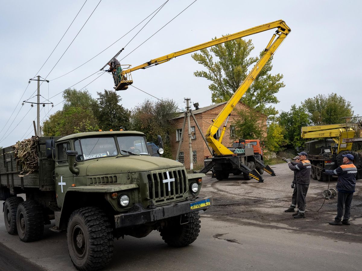 一辆乌克兰牌照的卡车，还有一辆樱桃采摘车。多名工人在电线杆上固定电线。