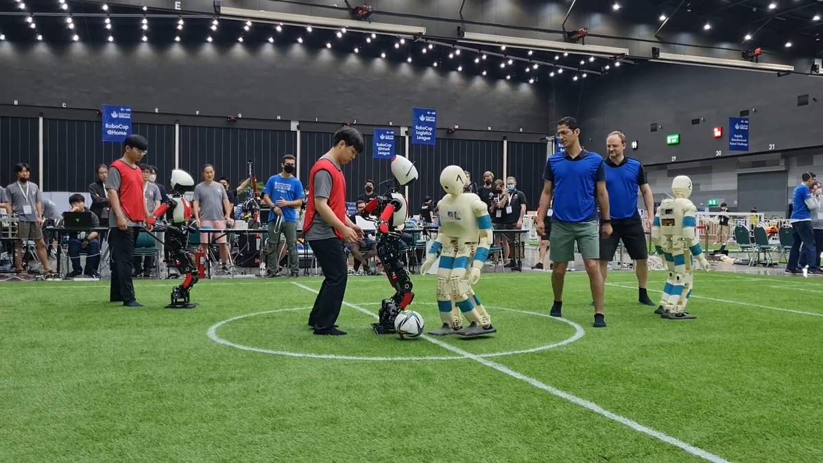 比赛开始时，人类和真人大小的人形机器人站在室内足球场上